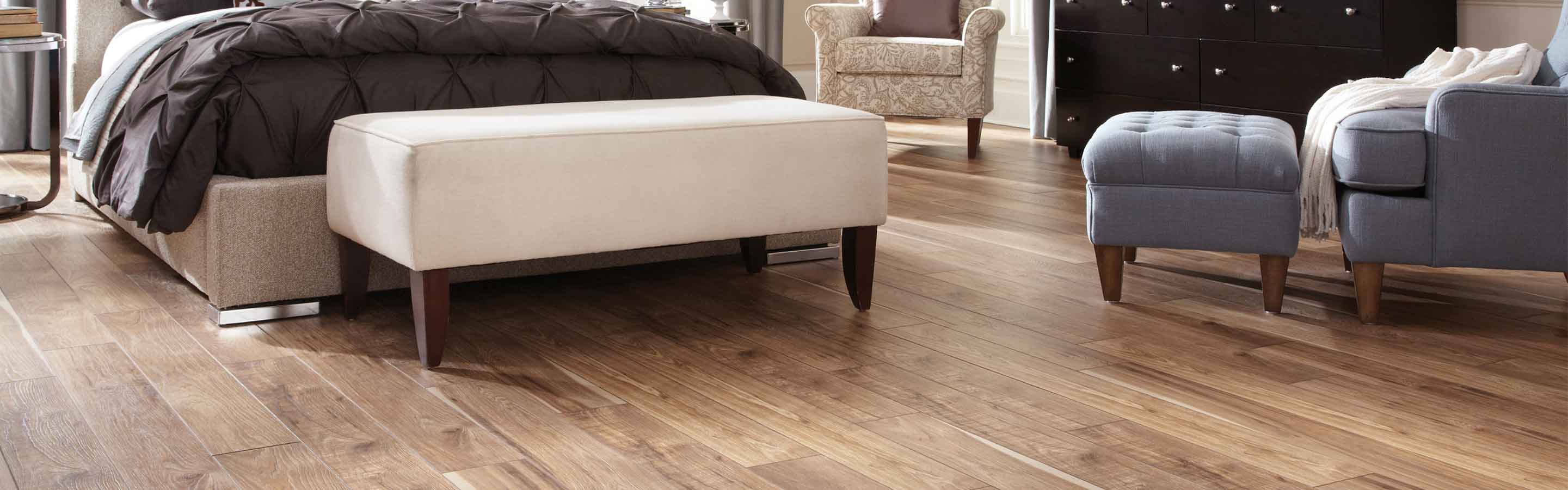 light wood-look laminate floors in contemporary bedroom with purple armchair, black wardrobe, and white bench